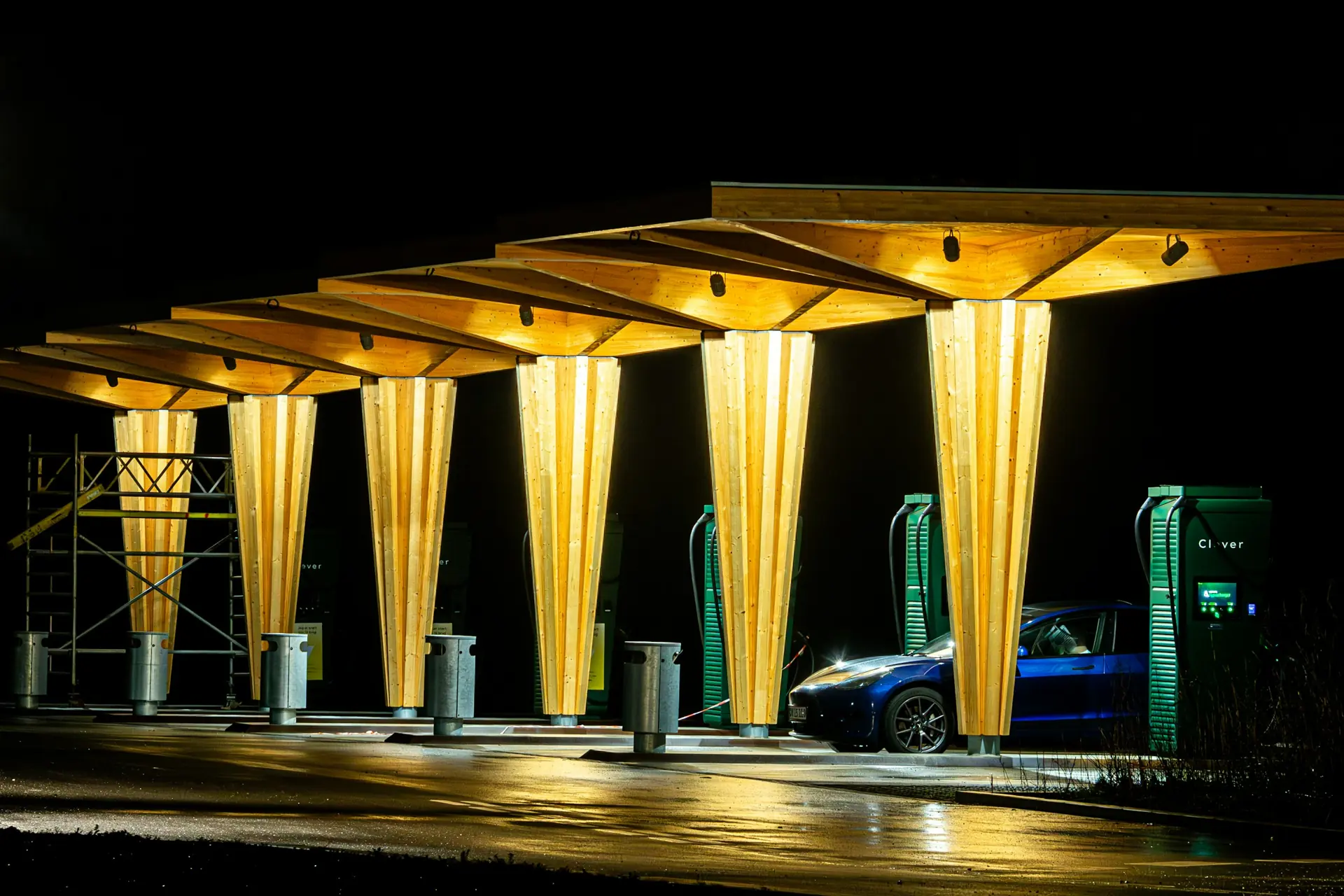 A modern EV charging station under a lit timber canopy at night